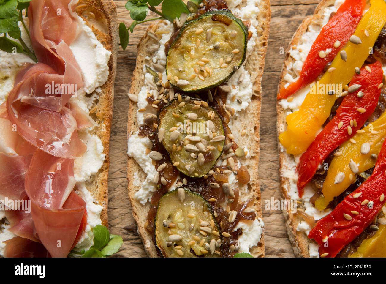 Three examples of bruschetta made with toasted sourdough bread spread with ricotta cheese. The toppings left-right are: Serrano ham drizzled with oliv Stock Photo