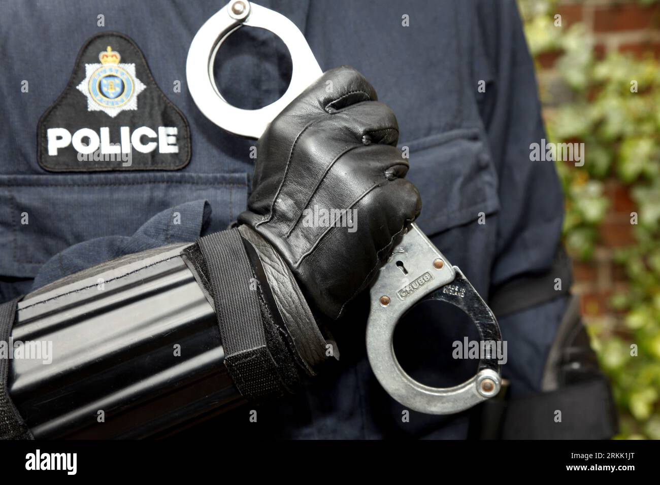 An adult male with his hands bound together by handcuffs and secured to his arm with police gloves Stock Photo