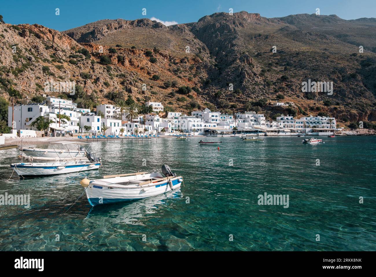 Small boats float on clear, emerald waters of the sea in the picturesque, white-washed village of Loutro, Crete. Stock Photo