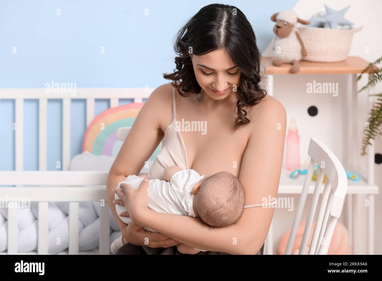 Young woman breastfeeding her baby in bedroom Stock Photo