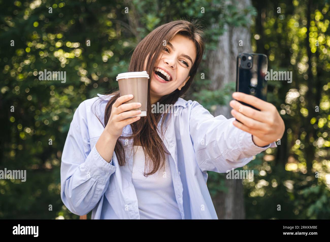 A young woman takes a selfie with a cup of coffee on the background of ...
