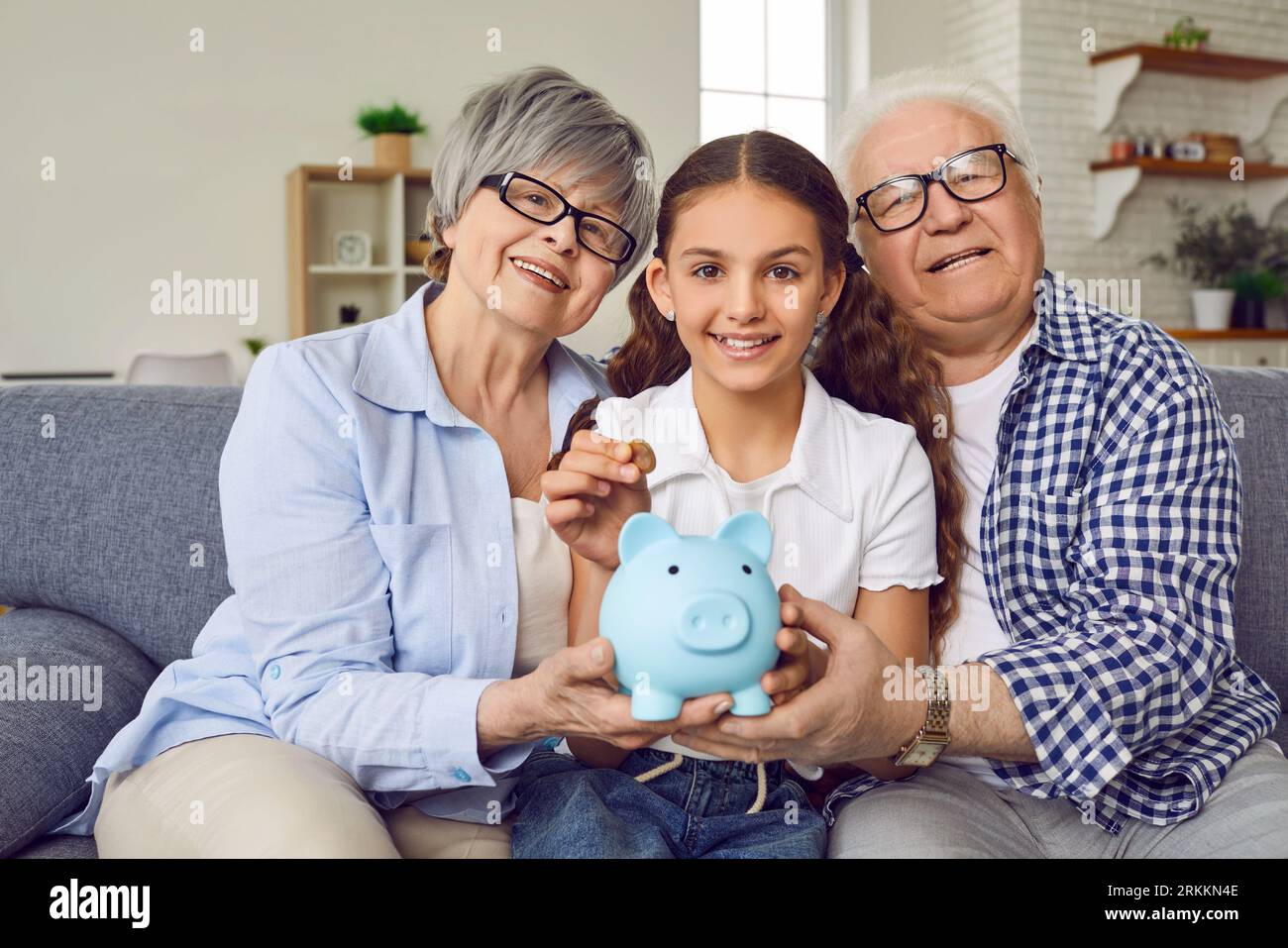 Happy grandchild together with grandmother and grandfather saves up money in piggy bank Stock Photo