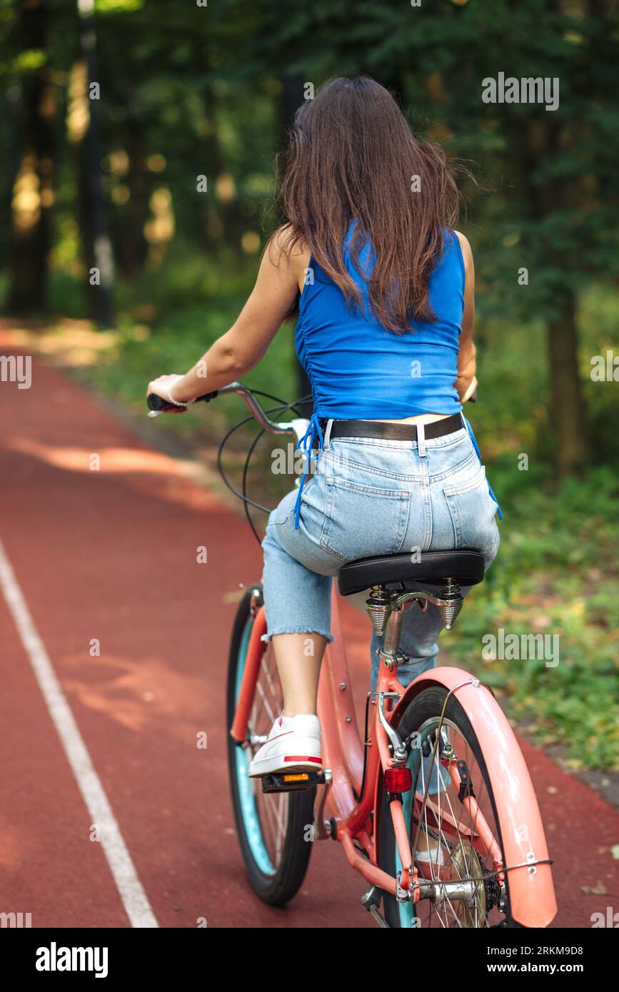 Woman riding bicycle on road in the summer park outdoors, back view Stock Photo