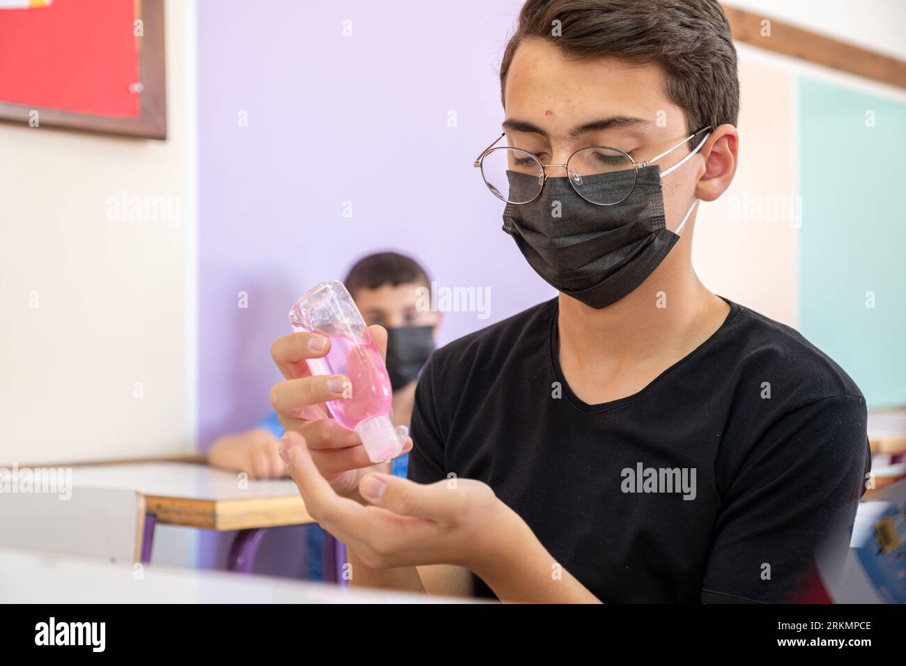 Teenager in school sterilizing his hands while wearing face mask to prevent infection Stock Photo