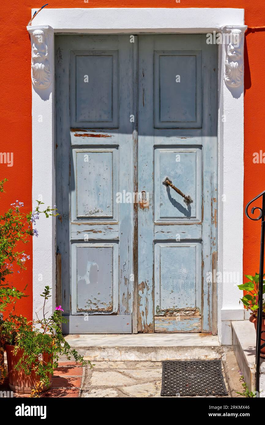 Traditional wooden door entrance with double doors, a stone built lintel and threshold, and a bright red wall, in Parga, Preveza, Greece Stock Photo
