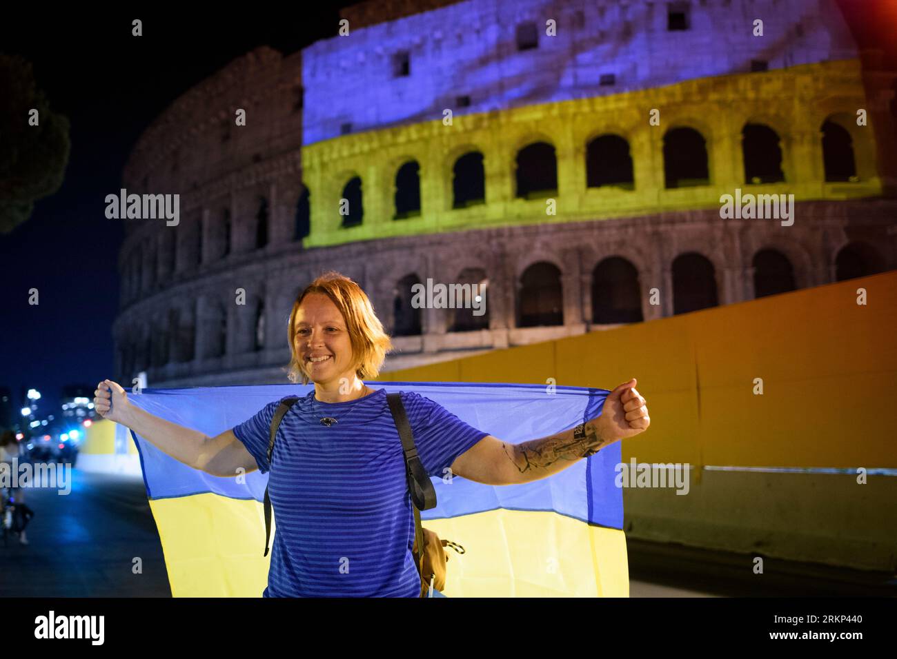Rome, Italy. 24th Aug, 2023. A woman poses for a souvenir photo with the Ukrainian flag on her shoulders in front of the Colosseum on which the Ukrainian flag is projected on the day of celebrating the Ukrainian independence from the USSR in Rome. On 24th August, Ukrainians celebrate Ukraine's Independence Day to commemorate the 1991 declaration of independence from the USSR. UNHCR estimates that around 6 million refugees have left Ukraine since the Russian invasion, about 170,000 would reside in Italy. (Credit Image: © Marcello Valeri/ZUMA Press Wire) EDITORIAL USAGE ONLY! Not for Commercia Stock Photo