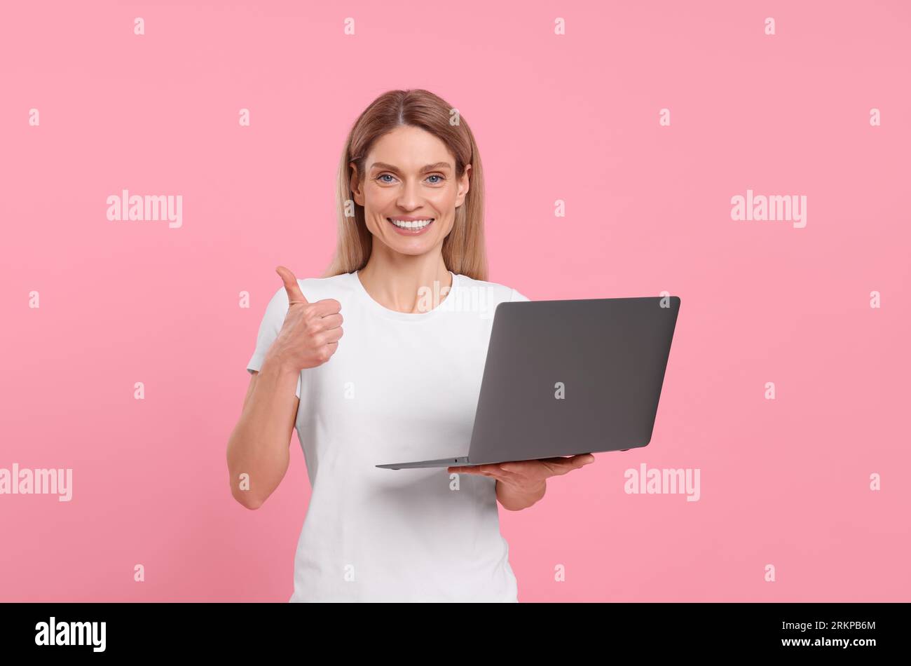 Happy woman with laptop showing thumb up on pink background Stock Photo ...