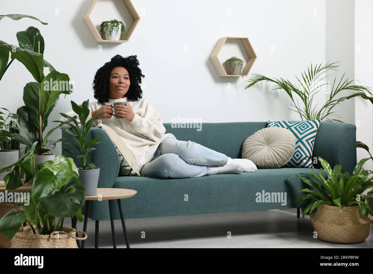 Relaxing atmosphere. Woman with cup of hot drink on sofa near beautiful ...