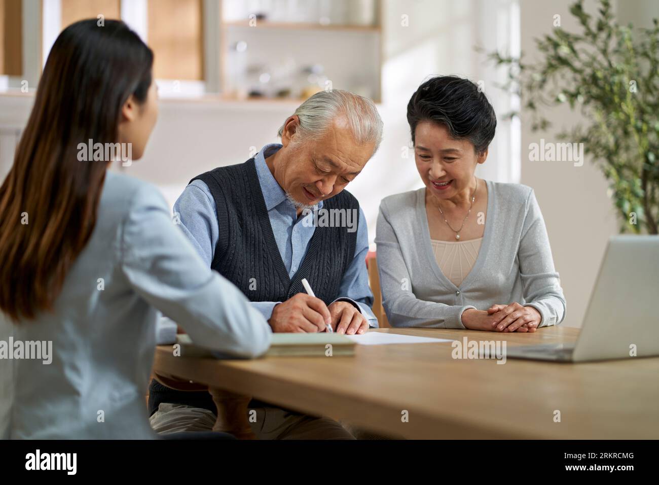 senior asian couple signing an agreement in front of a saleswoman at home Stock Photo