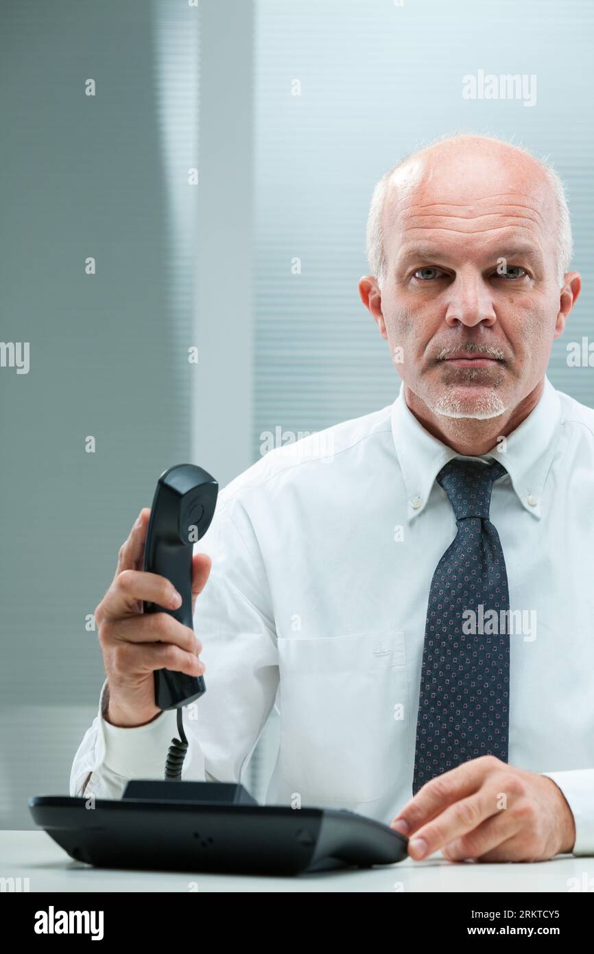 Immediate challenges demand direct intervention. A businessman in formal wear, seated by his computer, lifts the phone. The urgency and seriousness of Stock Photo