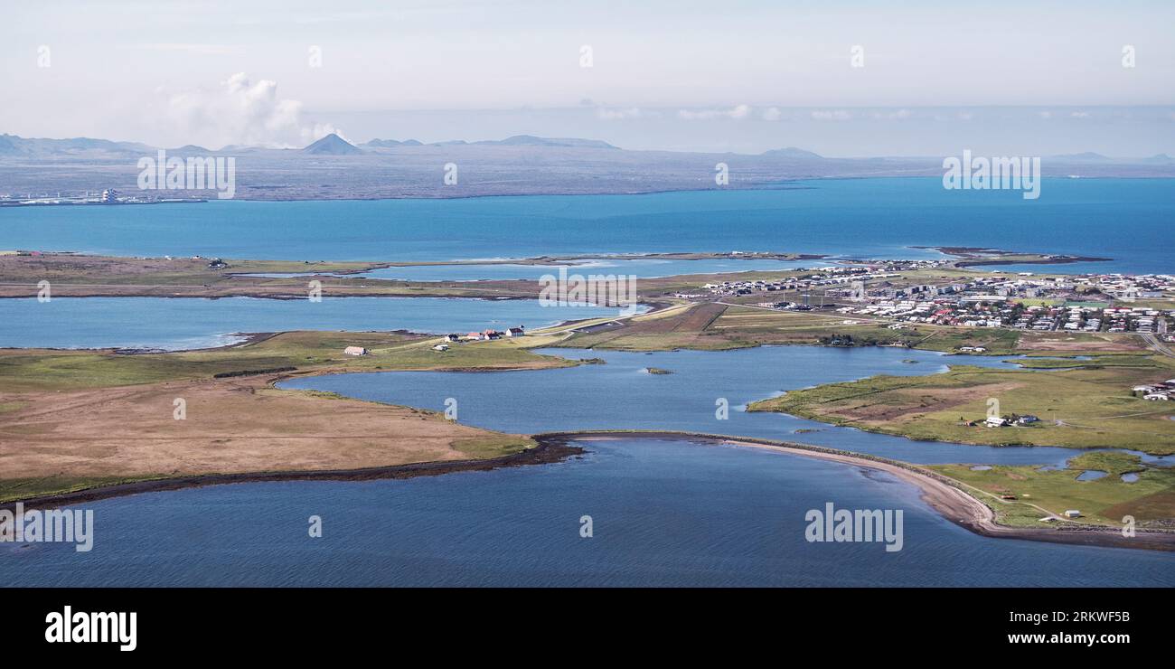 aerial photo of Reykjavik Iceland and the fjord and harbor with a still smoking volcano and hazy blue sky in the background Stock Photo