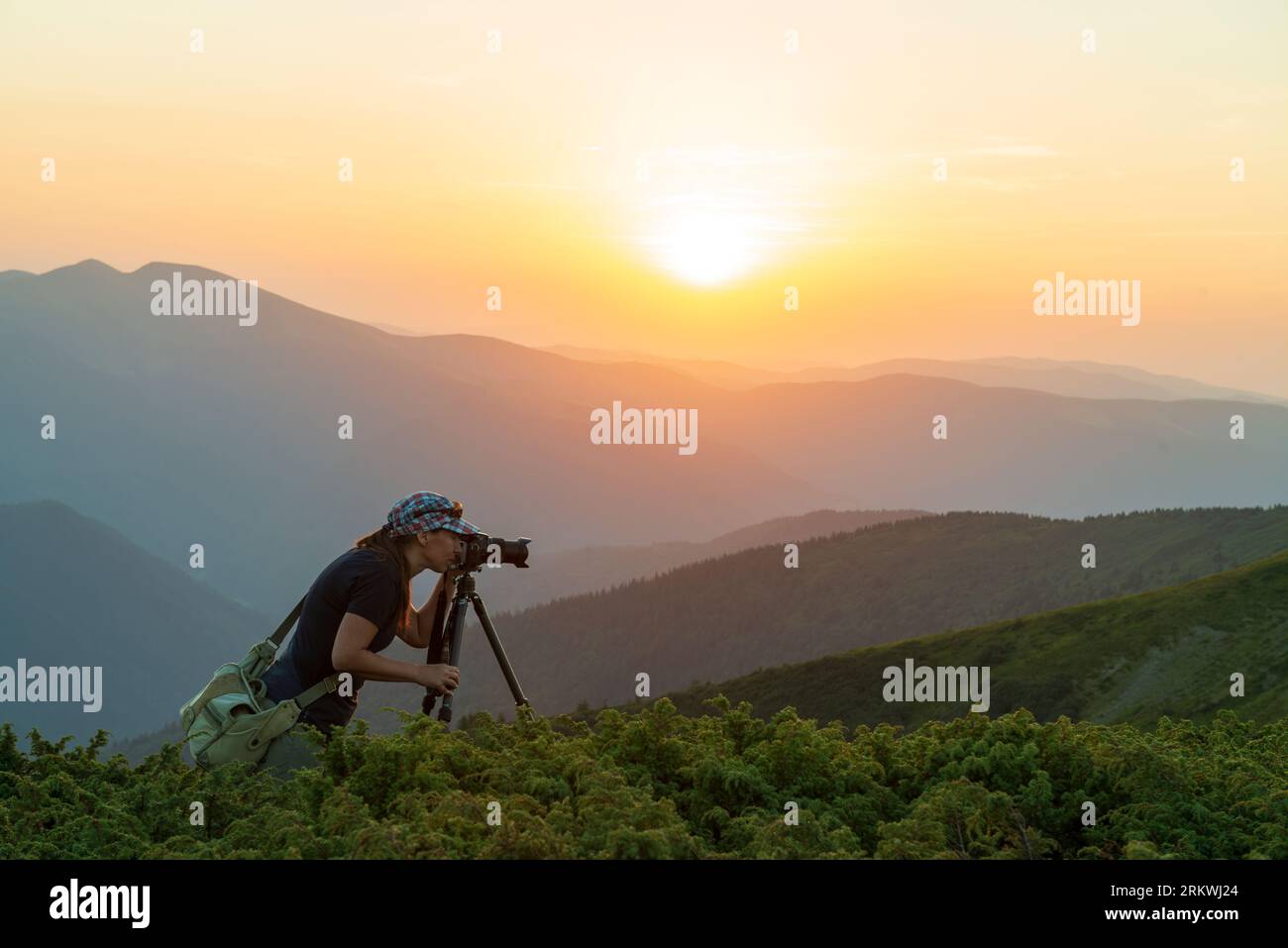 Girl photographer with tripod takes sunset photos high in the mouantains Stock Photo