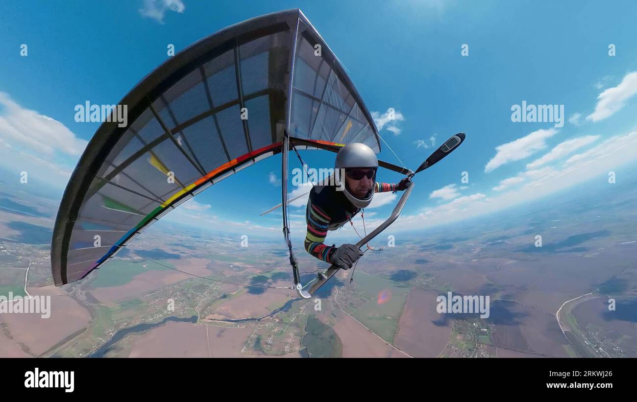 Hang glider pilot on the rainbow colored wing soars high in the sky Stock Photo