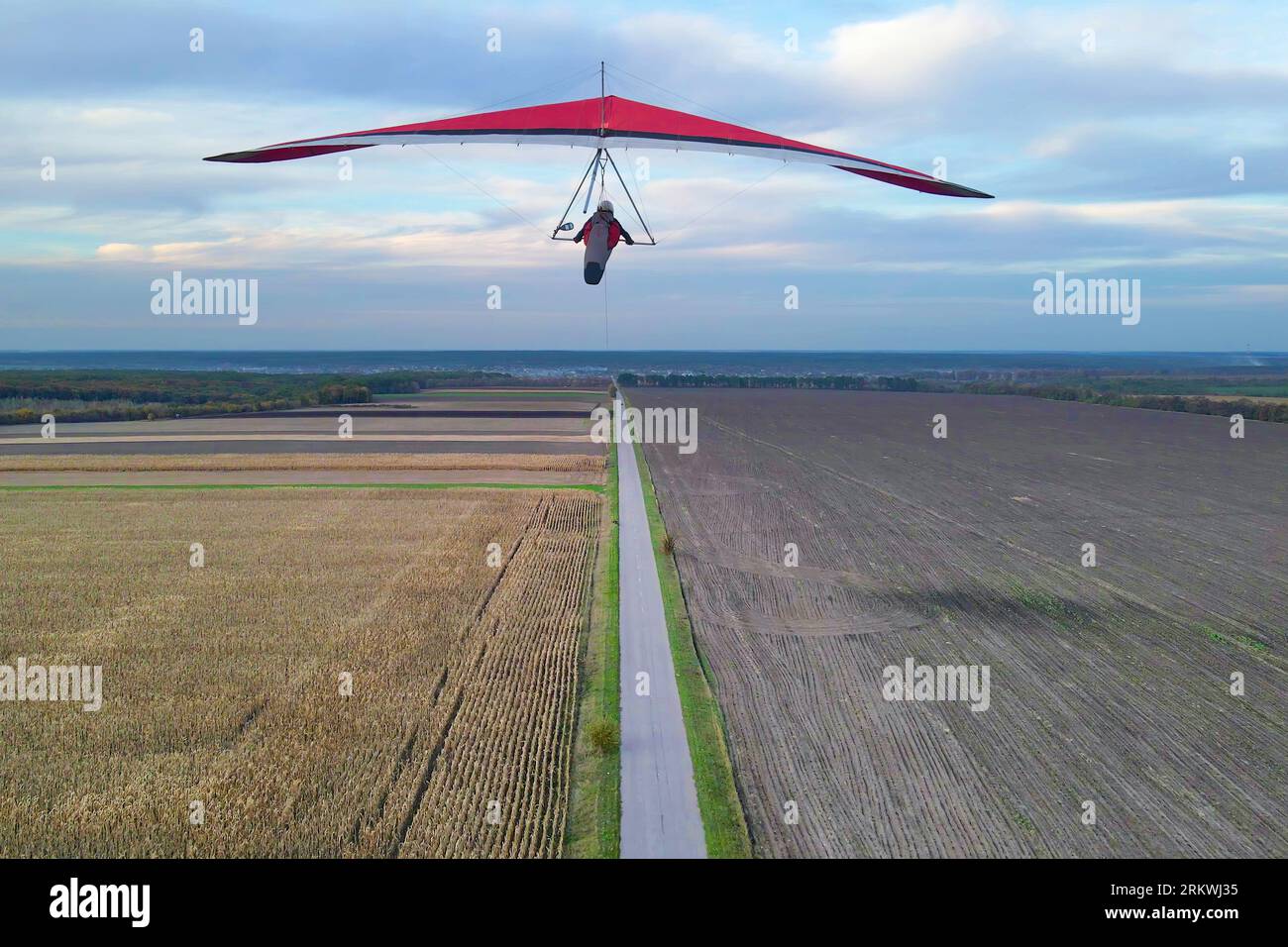 Red hang glider wing flies above the cultivated farm fields. Stock Photo