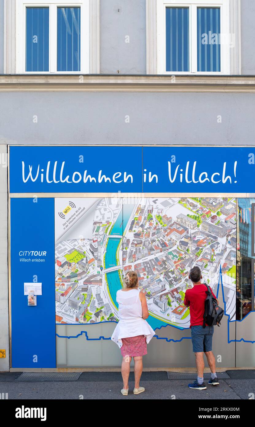 Villach, Austria - July 12, 2023: A tourist couple looking at a map of the city of Villach on the wall of the information office. German text translat Stock Photo