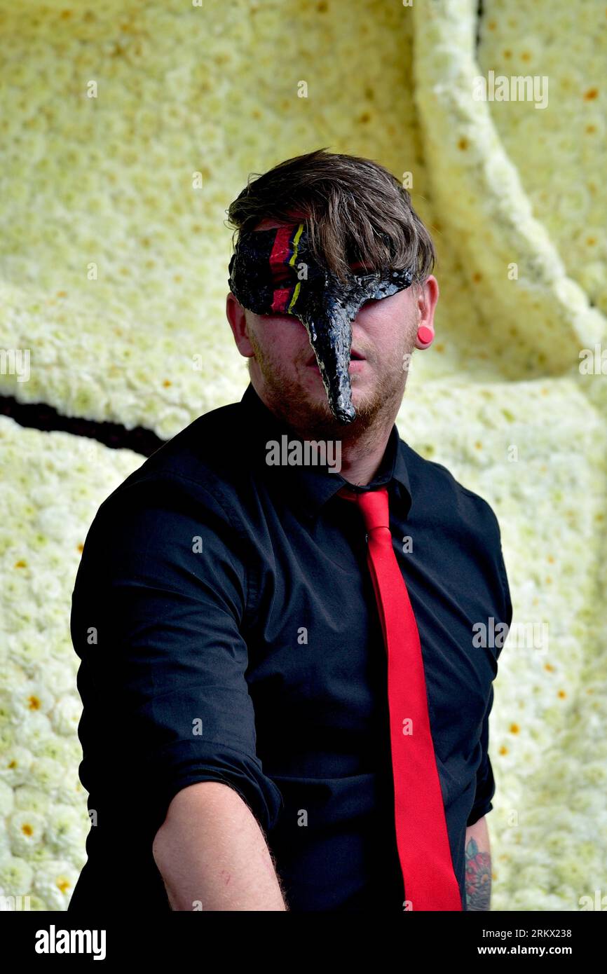 Man with a Venetian eye mask with a long-pointed nose performs a musical act on a float of one of the participants in the flower parade in Zundert Stock Photo