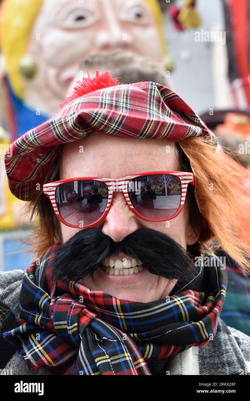 Portrait of a carnival-celebrating man with a tartan cap and scarf, a thick black mustache and red and white sunglasses, Breda Stock Photo