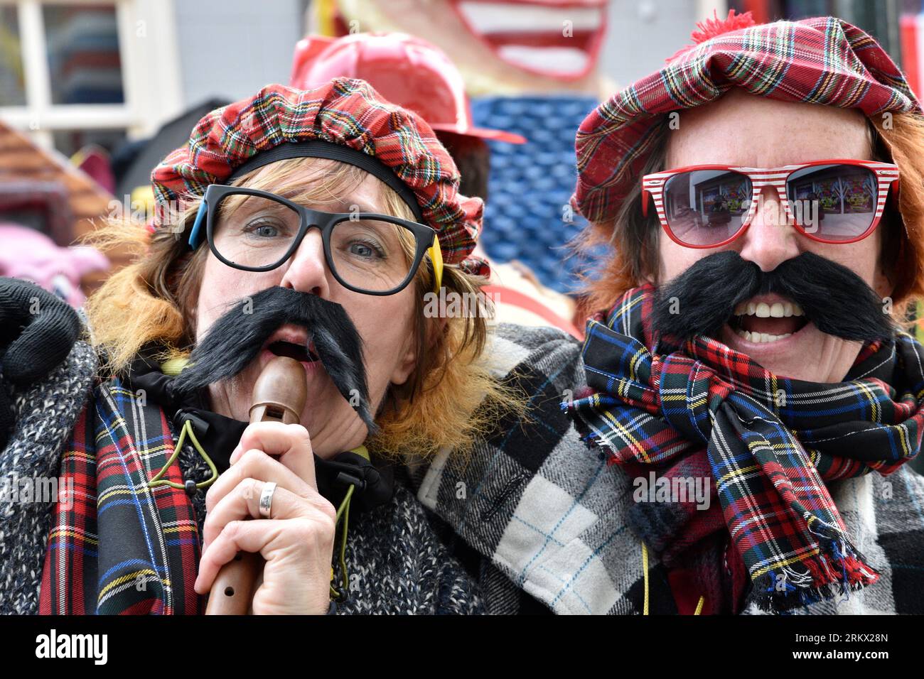 Two carnival celebrating people with big mustaches and glasses and caps and scarves in tartan on the swing in the Kielegat (Smockhole) Stock Photo