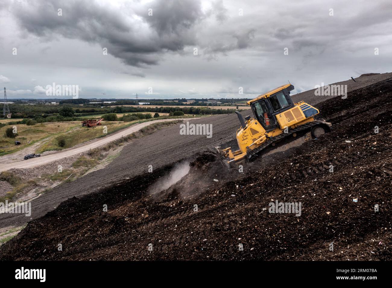 A bulldozer organising and moving shredded waste on the downhill slope of a large landfill site with copy space Stock Photo