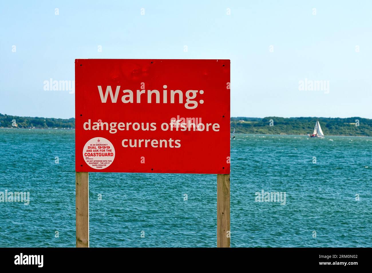 A large red sign on the beach warning the public of 'Dangerous Offshore Currents' at Lepe country park on a summers day Hampshire England UK Stock Photo