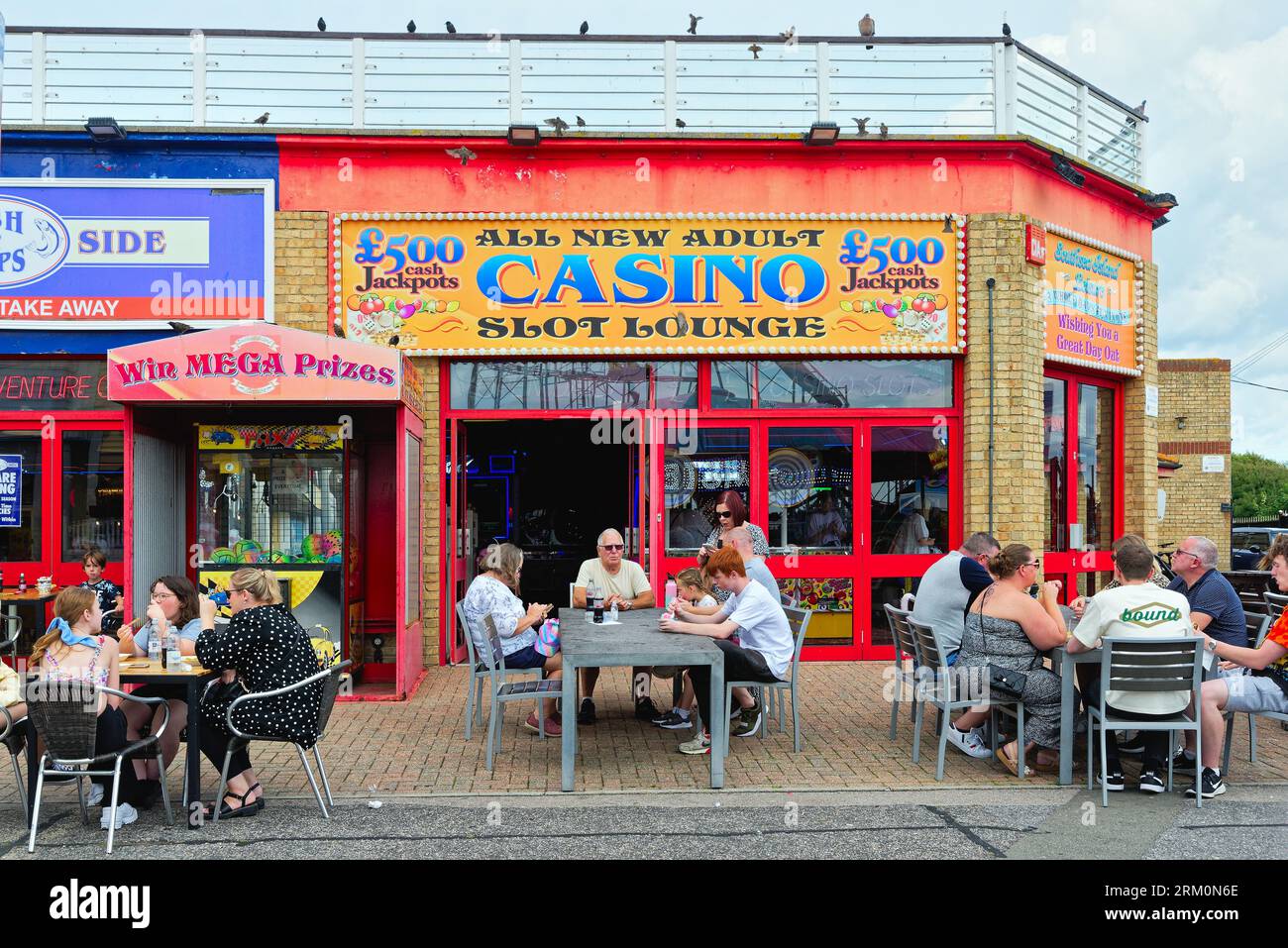 Families sitting at three  tables drinking and eating outside an amusement arcade on the seafront at Portsmouth Hampshire England UK Stock Photo