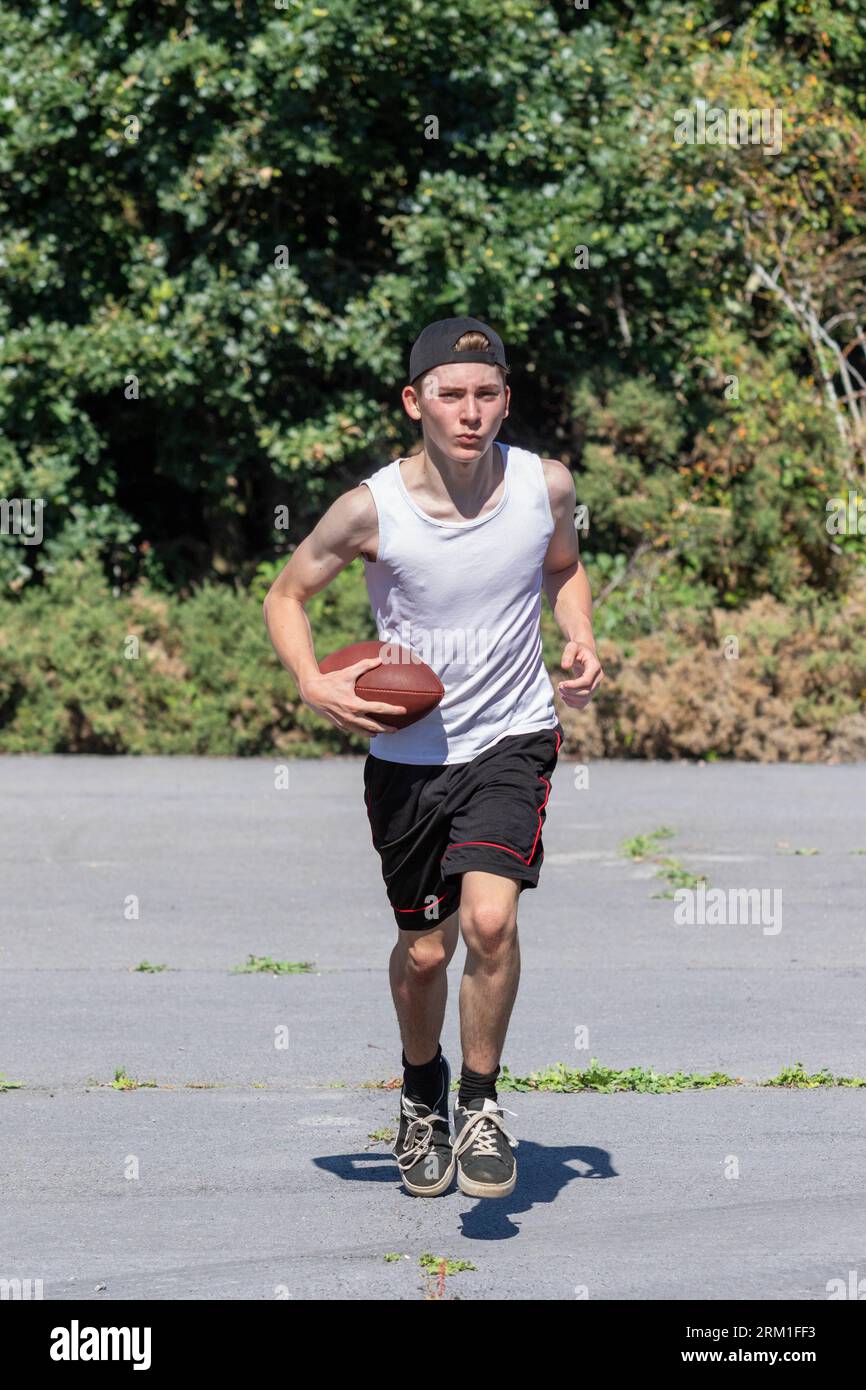Fit and active teenage boy running outside with an American Football Stock Photo