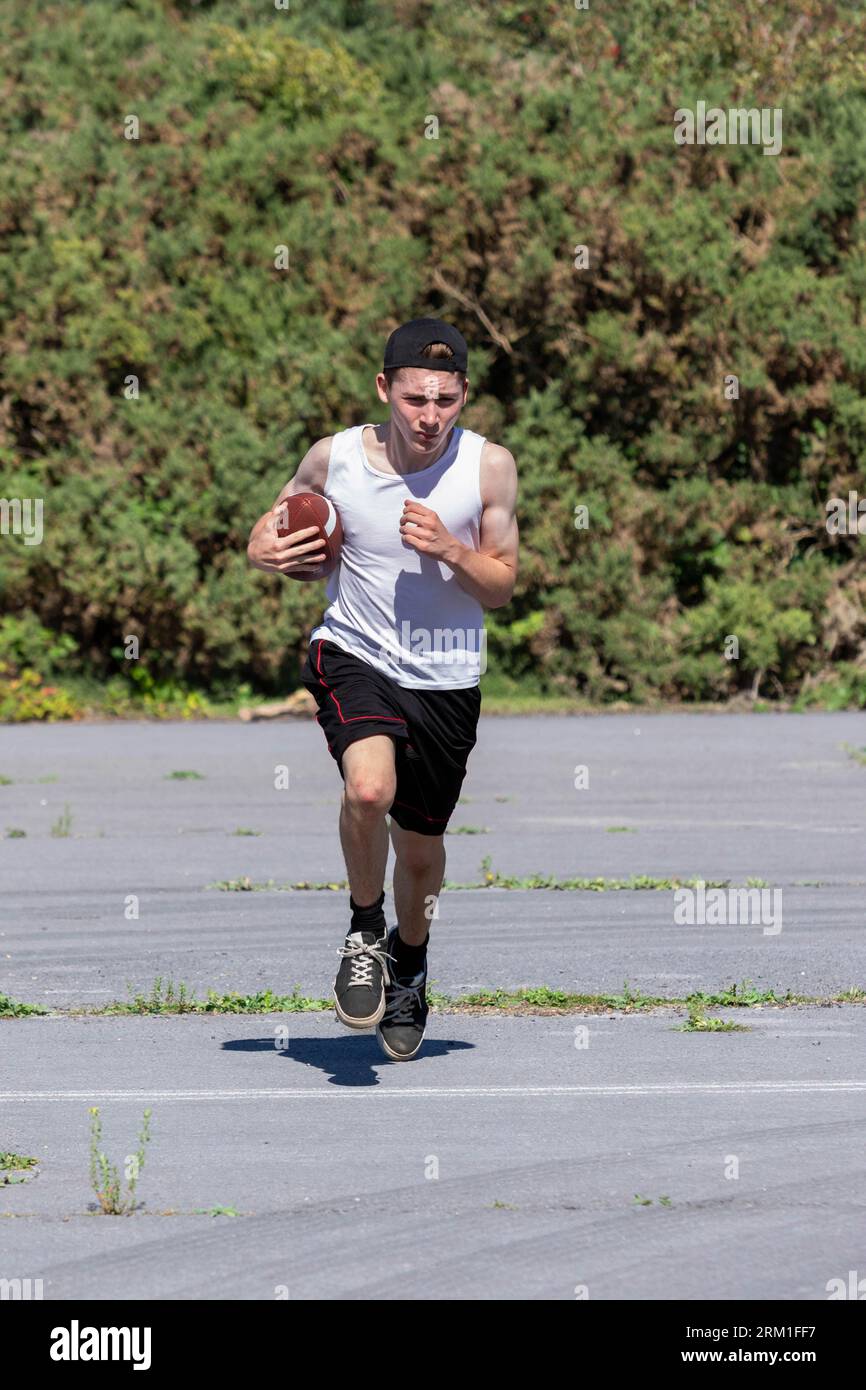 Fit and active teenage boy running outside with an American Football Stock Photo