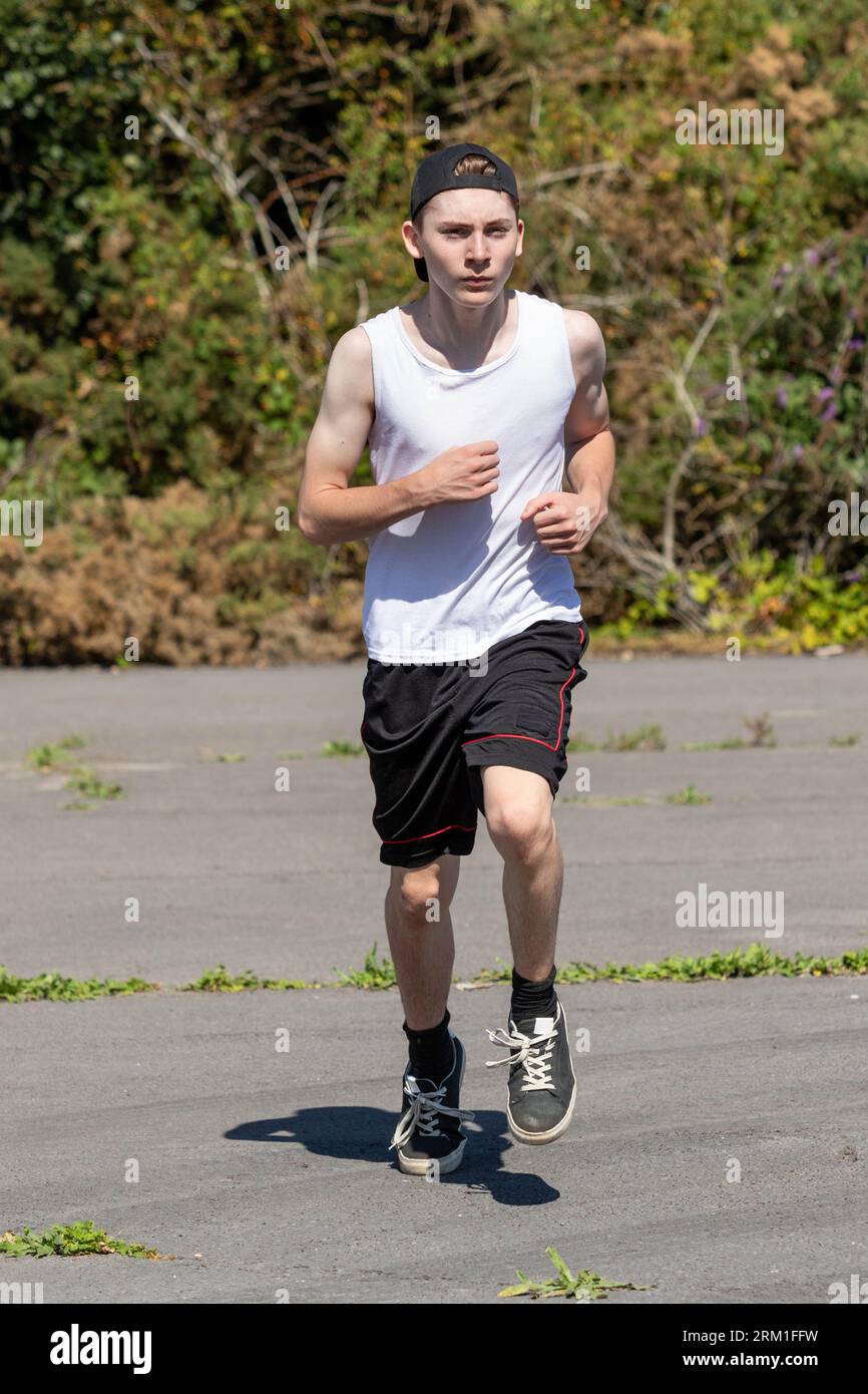 Fit and sporty teenage boy wearing a cap backwards, running during a