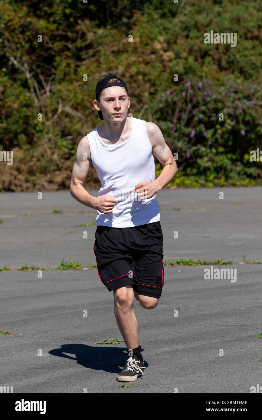 Fit and sporty teenage boy wearing a cap backwards, running during a