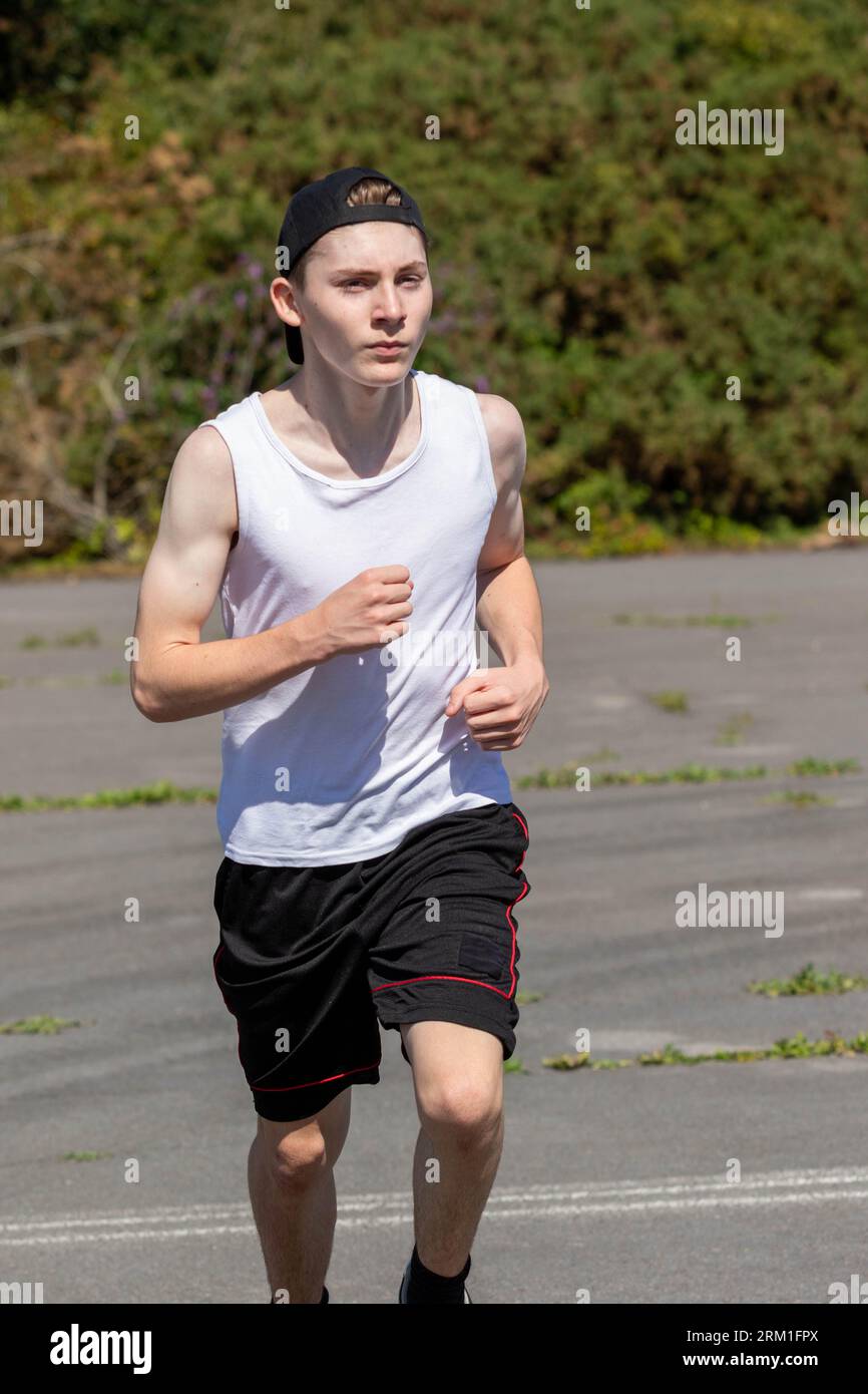 Fit and sporty teenage boy wearing a cap backwards, running during a