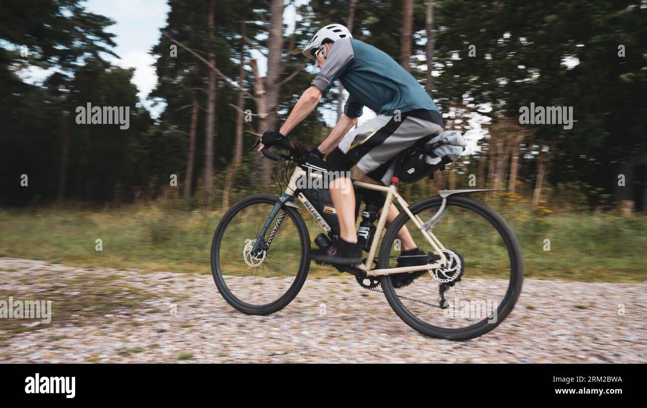 A man rides a bikepacking bike at speed on a gravel track in Thetford Forest in Norfolk, England UK Stock Photo