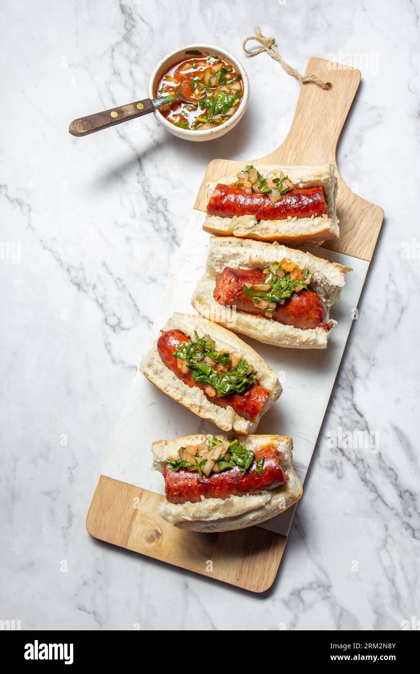 Chilean and Argentinian food. Traditional choripan with spicy pebre, chorizo sandwich with chorizo sausages and bread. Stock Photo
