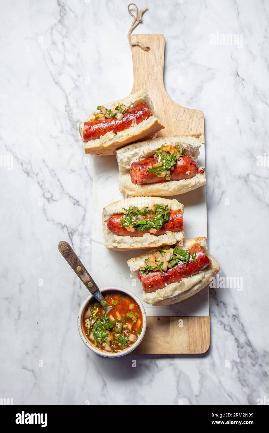 Chilean and Argentinian food. Traditional choripan with spicy pebre, chorizo sandwich with chorizo sausages and bread. Stock Photo