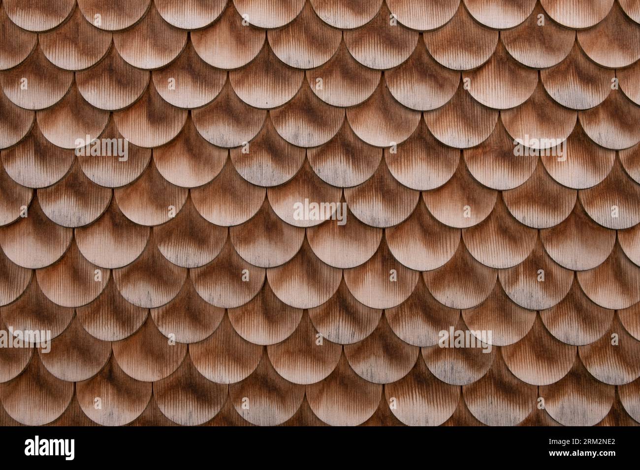Wooden round bottom shingles of wall siding of historic farmhouse. Wood shingle pattern, roof or facade. Traditional wooden architecture texture. Stock Photo
