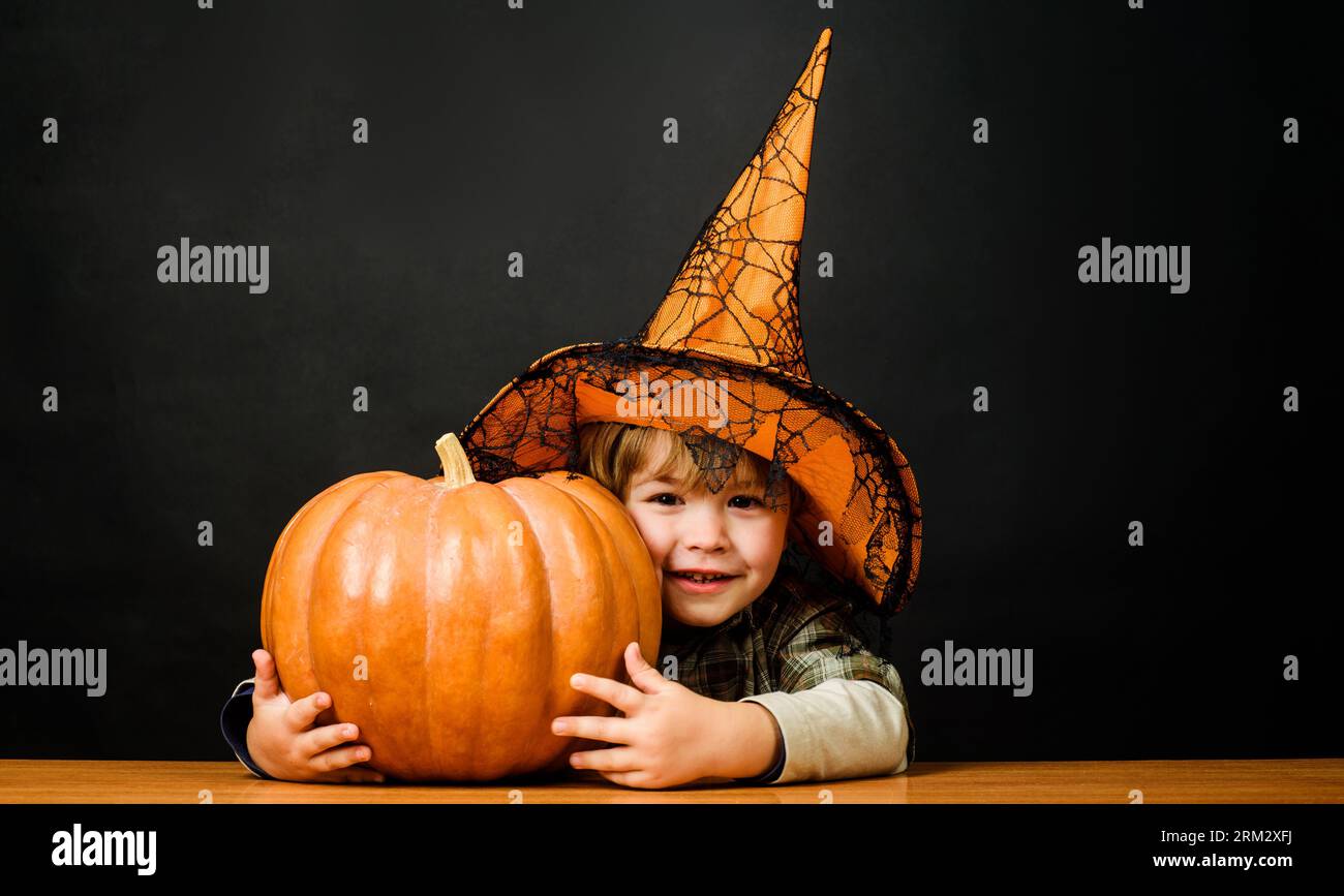 Halloween child in witch hat with pumpkin. Little kid in wizards costume with Halloween jack-o-lantern. Smiling boy in magic hat with halloween Stock Photo