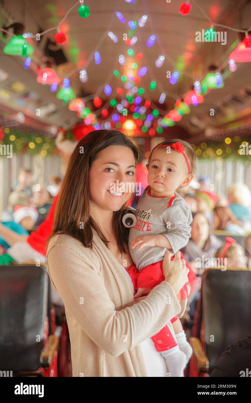 Mother holding beautiful baby girl with colorful christmas lights in the background on train or bus Stock Photo
