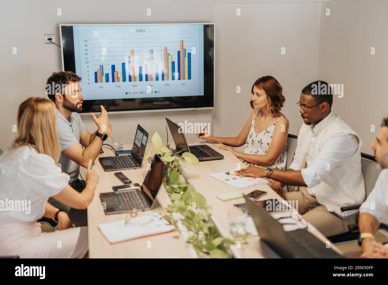 A diverse group of business employees in an office, analyzing statistics, discussing profit growth, and collaborating on project development and marke Stock Photo