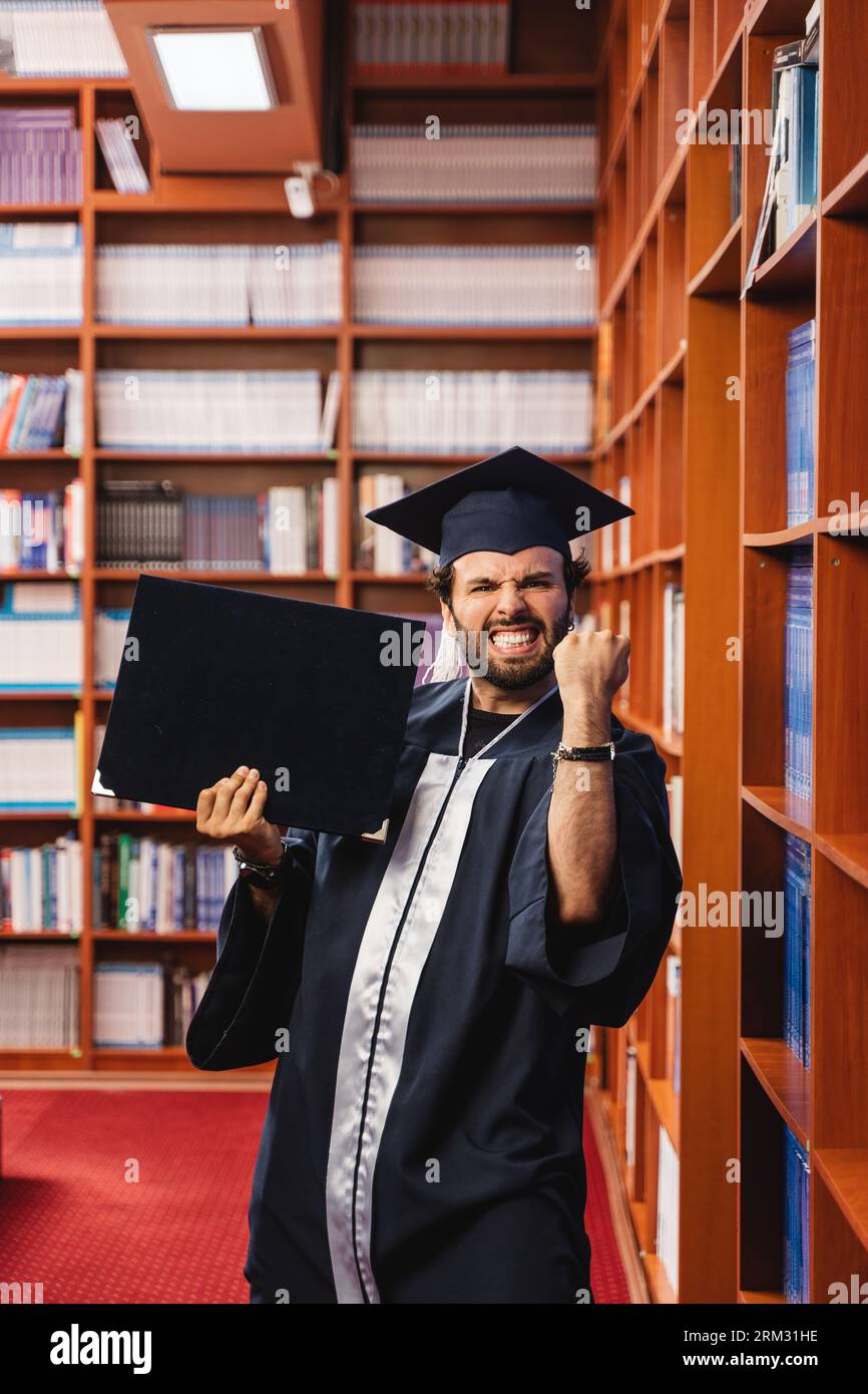Young and excited graduate wearing a cap and gown while holding his ...