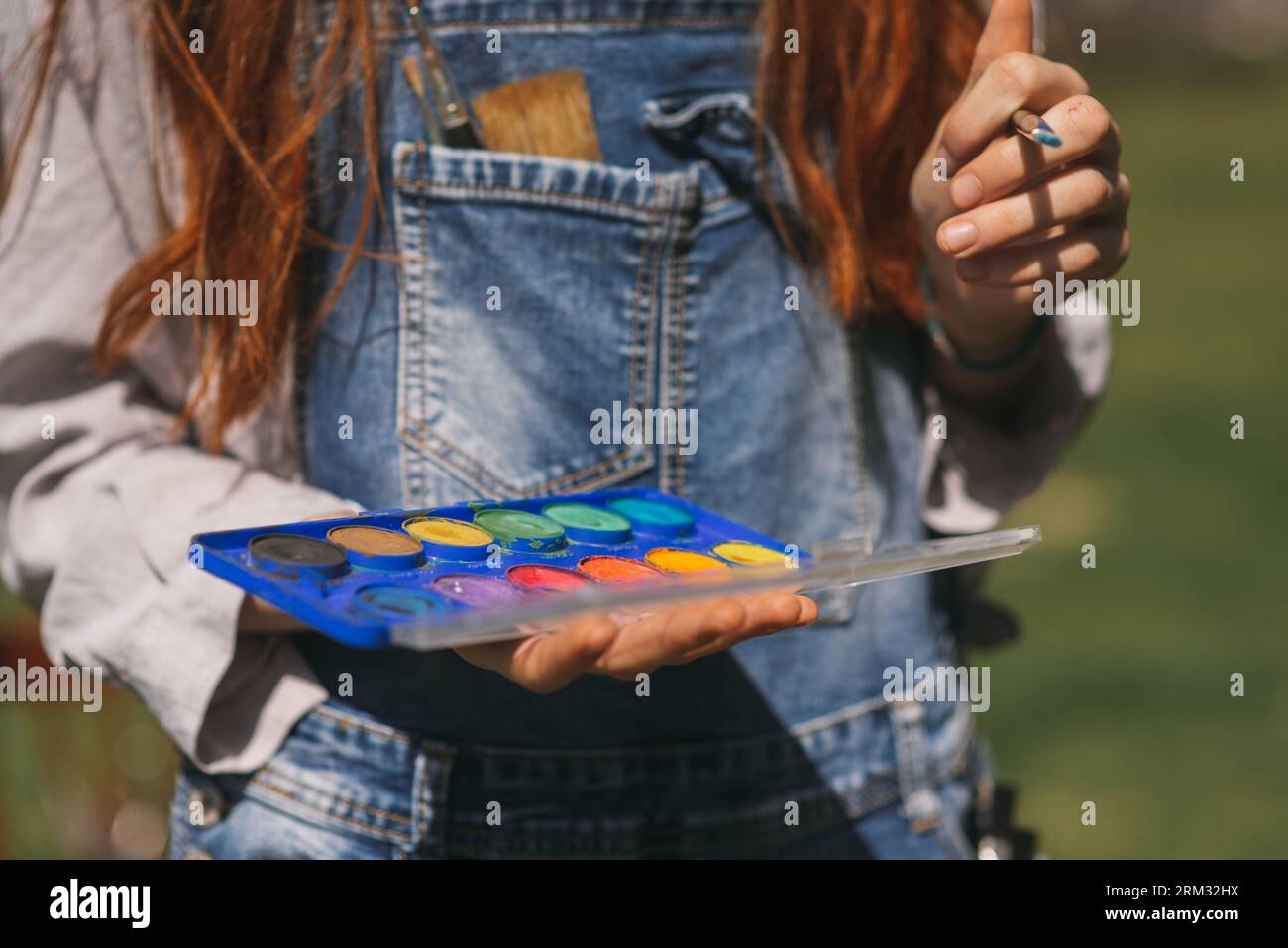 Red haired female artist holding a color palette in her hand and brush ...
