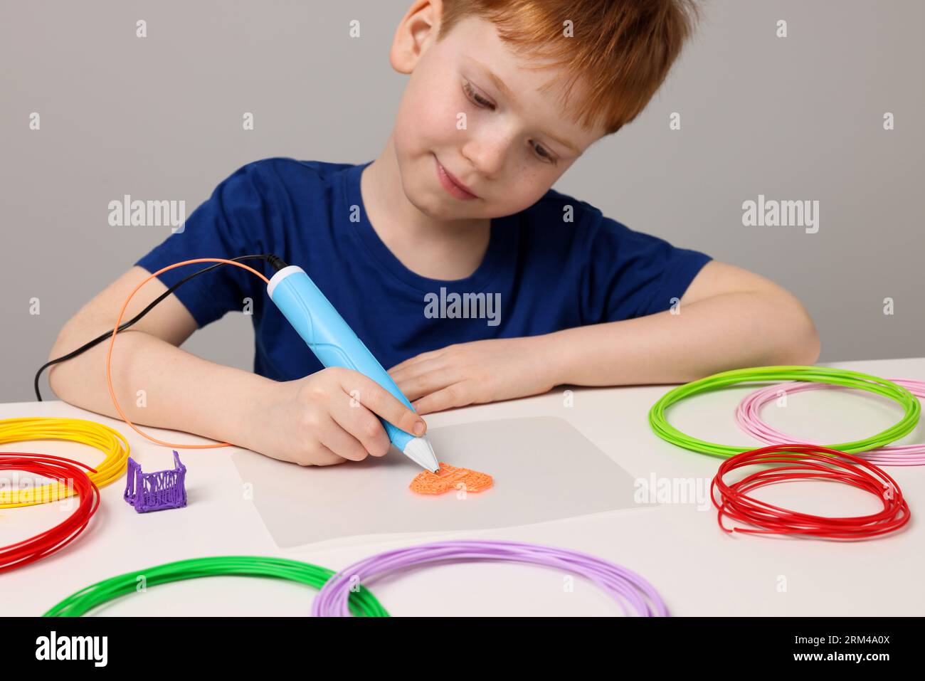 Boy drawing with stylish 3D pen at white table Stock Photo