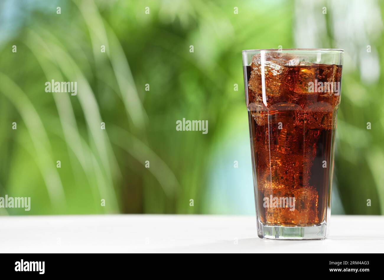 Glass of refreshing soda water with ice cubes on white table outdoors ...