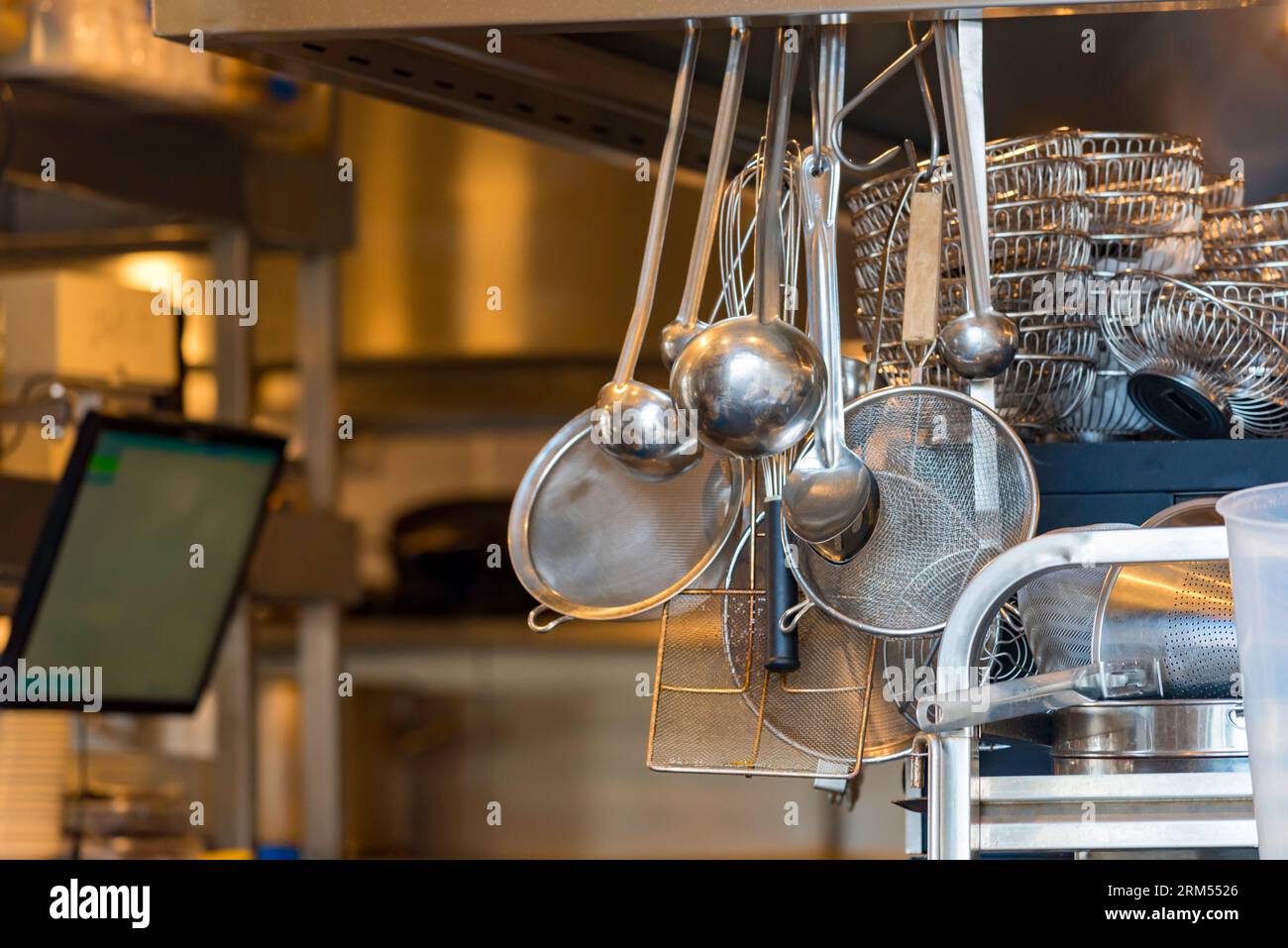 Stainless steel scoops, strainers and other utensils hanging in the doorway of a professional kitchen in Sydney, Australia Stock Photo