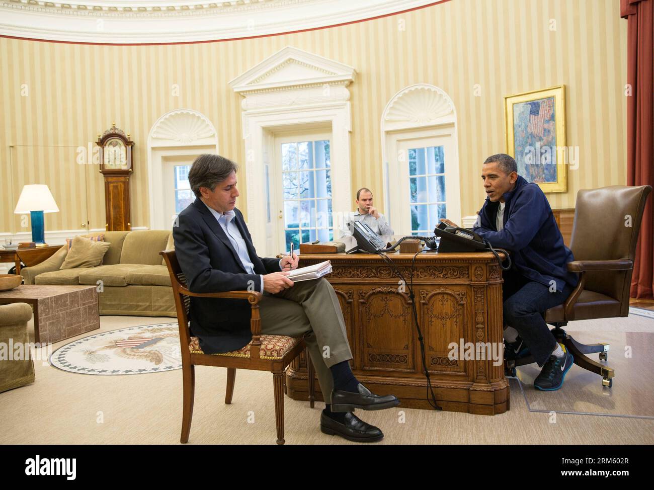 In this photo released by the White House, U.S. President Barack Obama R talks on a conference call with U.S. negotiators in Geneva, and Deputy National Security Advisors Tony Blinken L and Ben Rhodes C in the Oval Office, to discuss negotiations with Iran, in the Oval Office of the White House in Washington D.C., capital of the United States, Nov. 23, 2013. U.S. President Barack Obama on Saturday pledged no more sanctions on Iran after the Islamic republic closed a first-step deal with the six major nations on its nuclear program, but acknowledged huge challenges ahead in talks about reaching Stock Photo