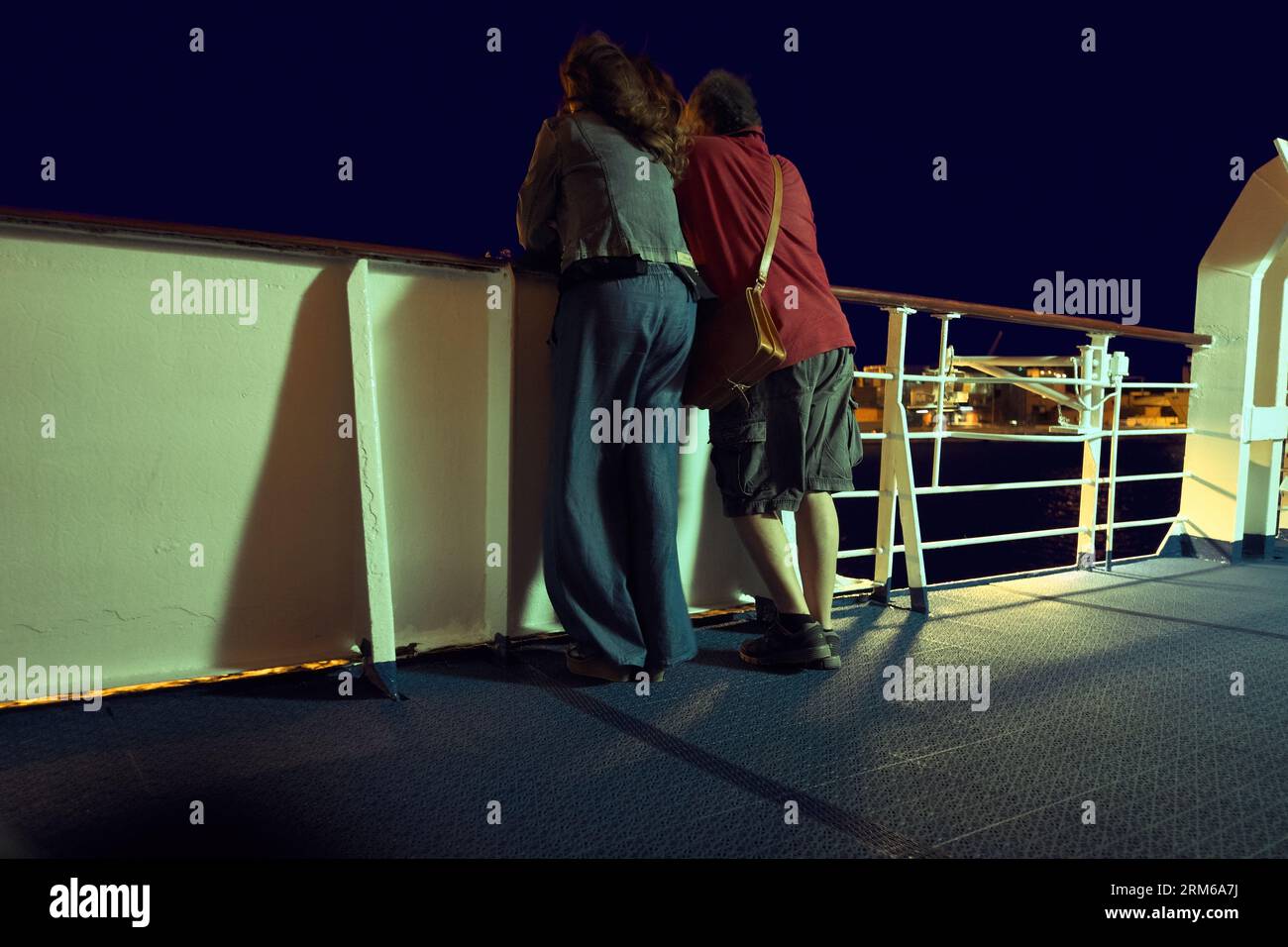 at night a couple looks out from the deck of a ship leaving for the Balkans from the port of Bari, Italy Stock Photo