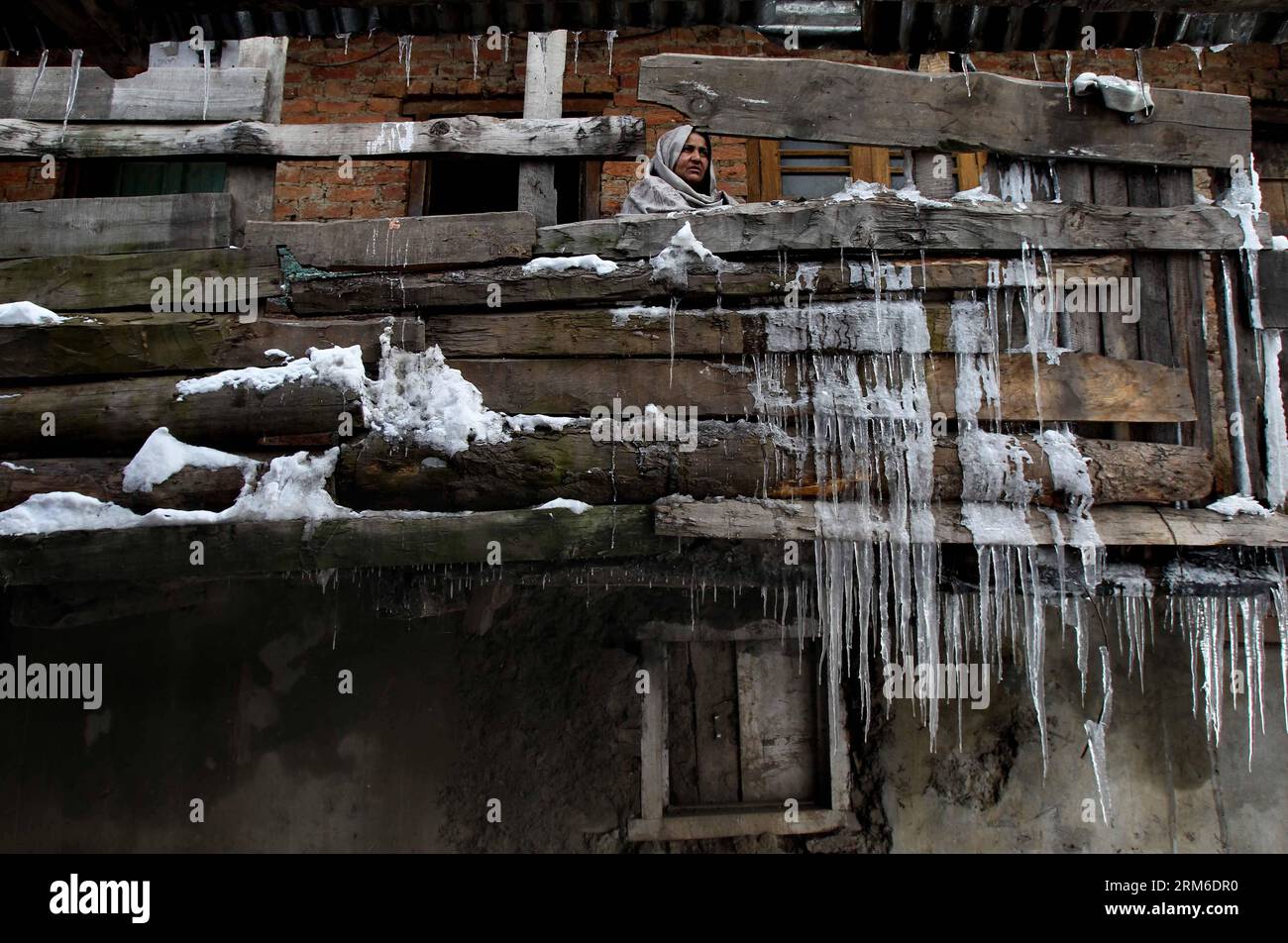 (140106) -- SRINAGAR, Jan. 6, 2014 (Xinhua) -- A Kashmiri woman looks on from her house with icicles hanging from the wooden fencing at Kokernag, about 80 kilometers south of Srinagar city, the summer capital of Indian-controlled Kashmir, Jan. 6, 2014. The colder parts of Indian-controlled Kashmir last week received a heavy snowfall, which suspended road, rail and air traffic to the region. The region is in the grip of cold wave and local meteorological department have predicted more snow on Wednesday. (Xinhua/Javed Dar) KASHMIR-SRINAGAR-SNOW-WEATHER PUBLICATIONxNOTxINxCHN   Srinagar Jan 6 201 Stock Photo