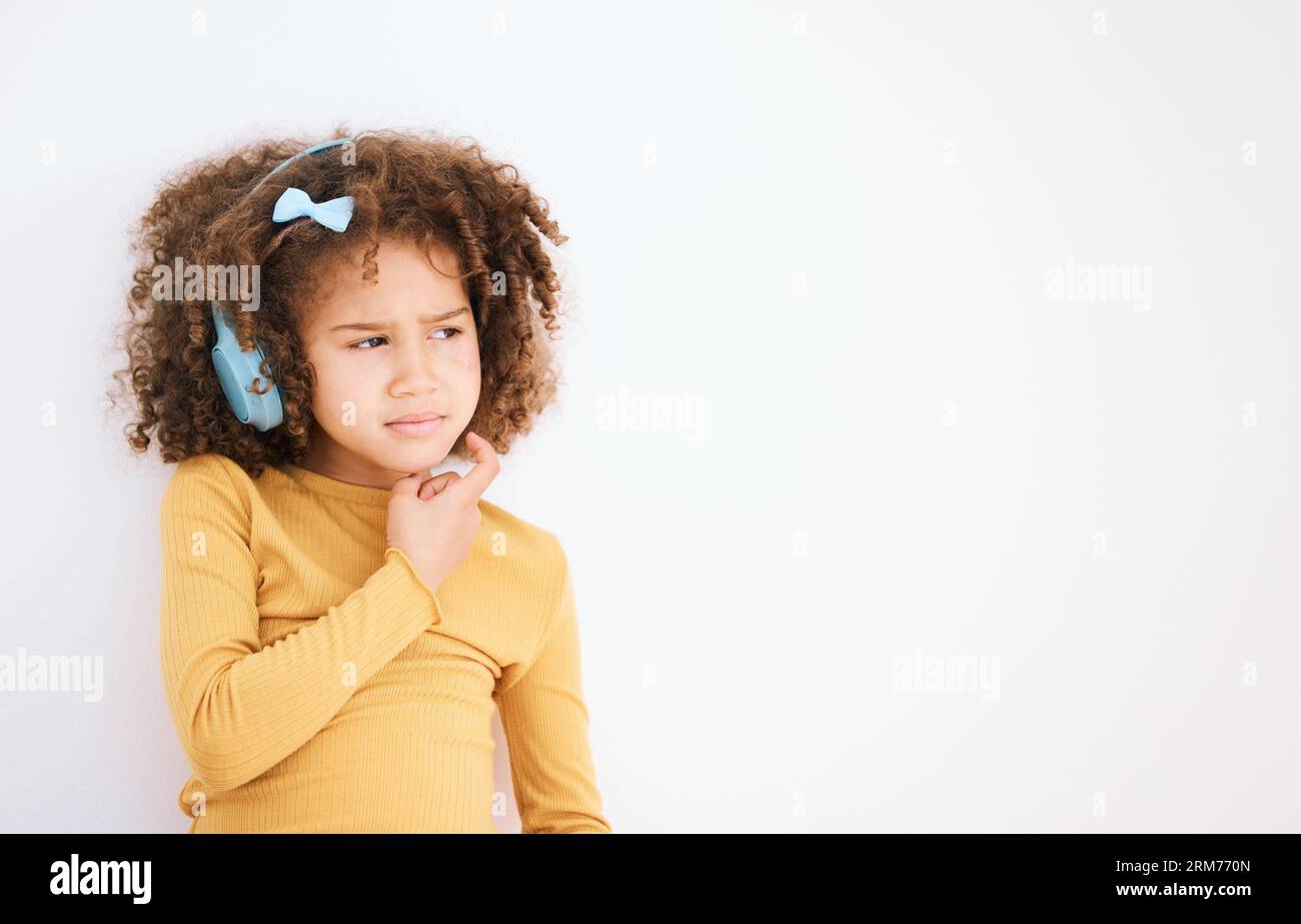 Thinking, problem and child with headphones on white background for planning, solution or music. Mockup, stress and a girl kid with a podcast, radio Stock Photo