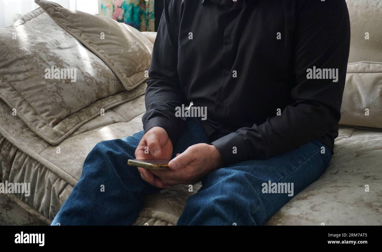 man sitting on sofa and looking at smartphone Stock Photo