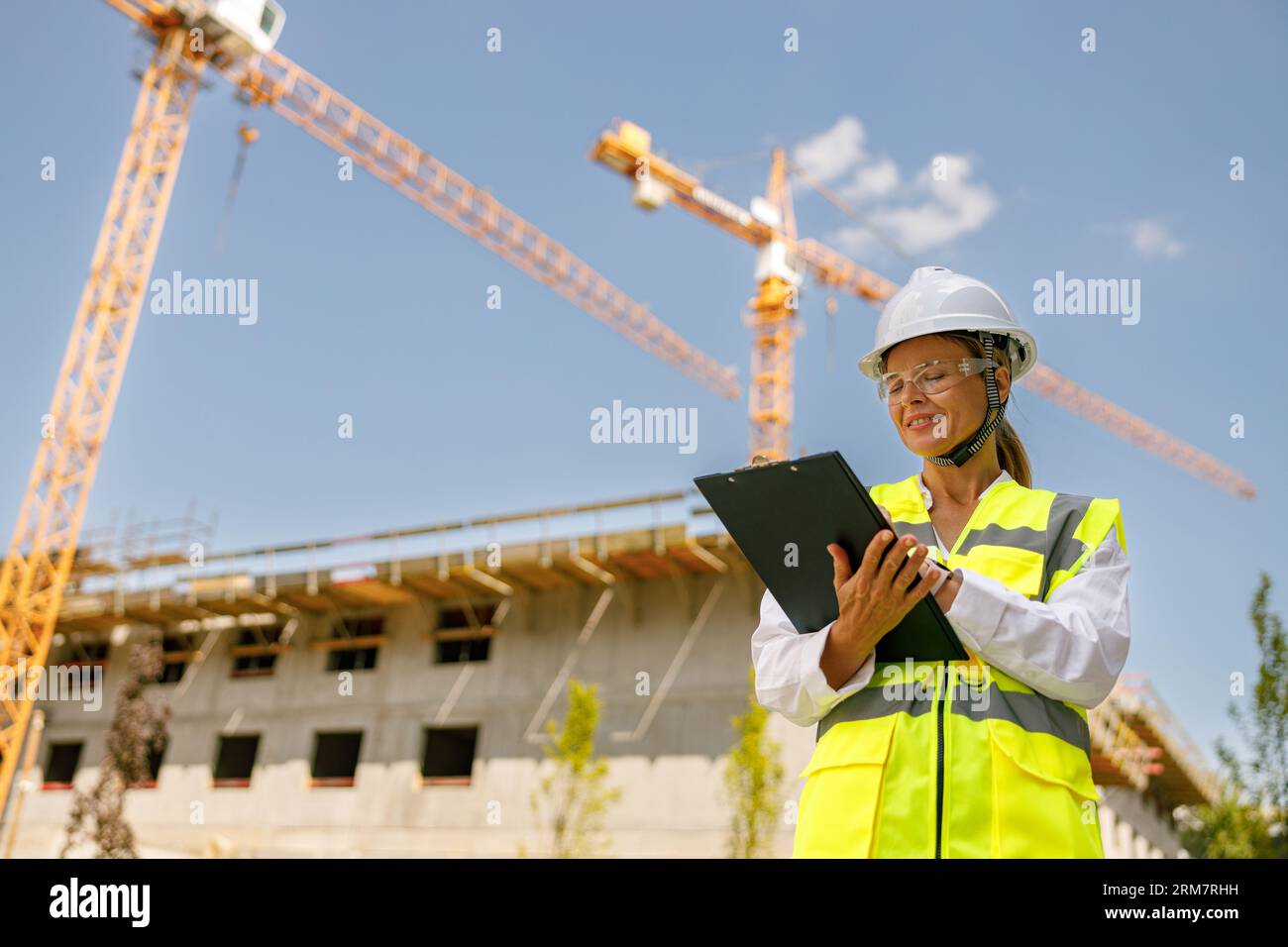 Professional female engineer in protective helmet making notes on construction site Stock Photo
