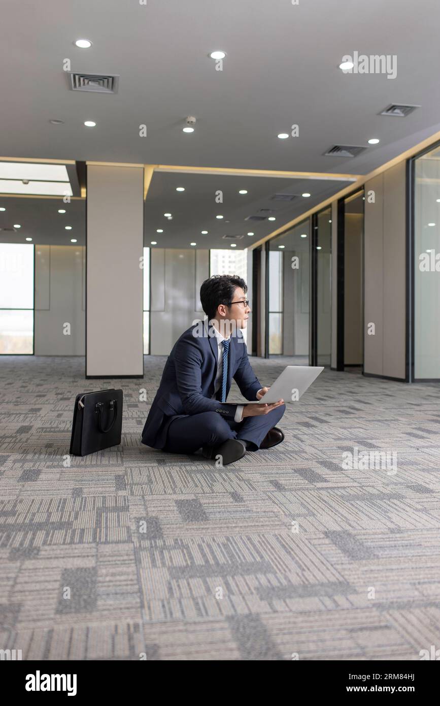Businessman using laptop on floor in empty office Stock Photo