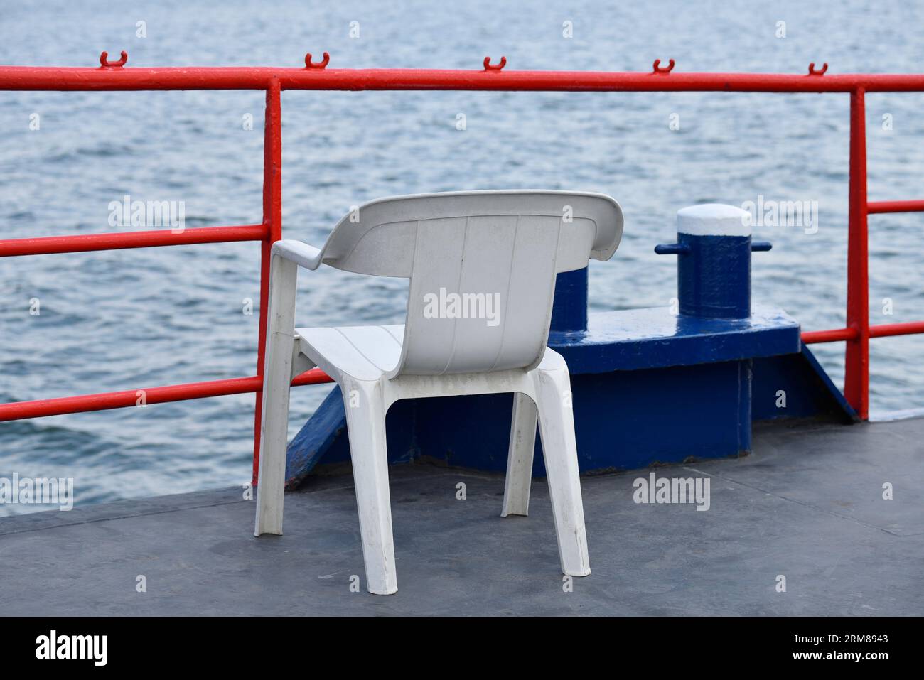 White plastic armchair stands on the boat on a red railing and against